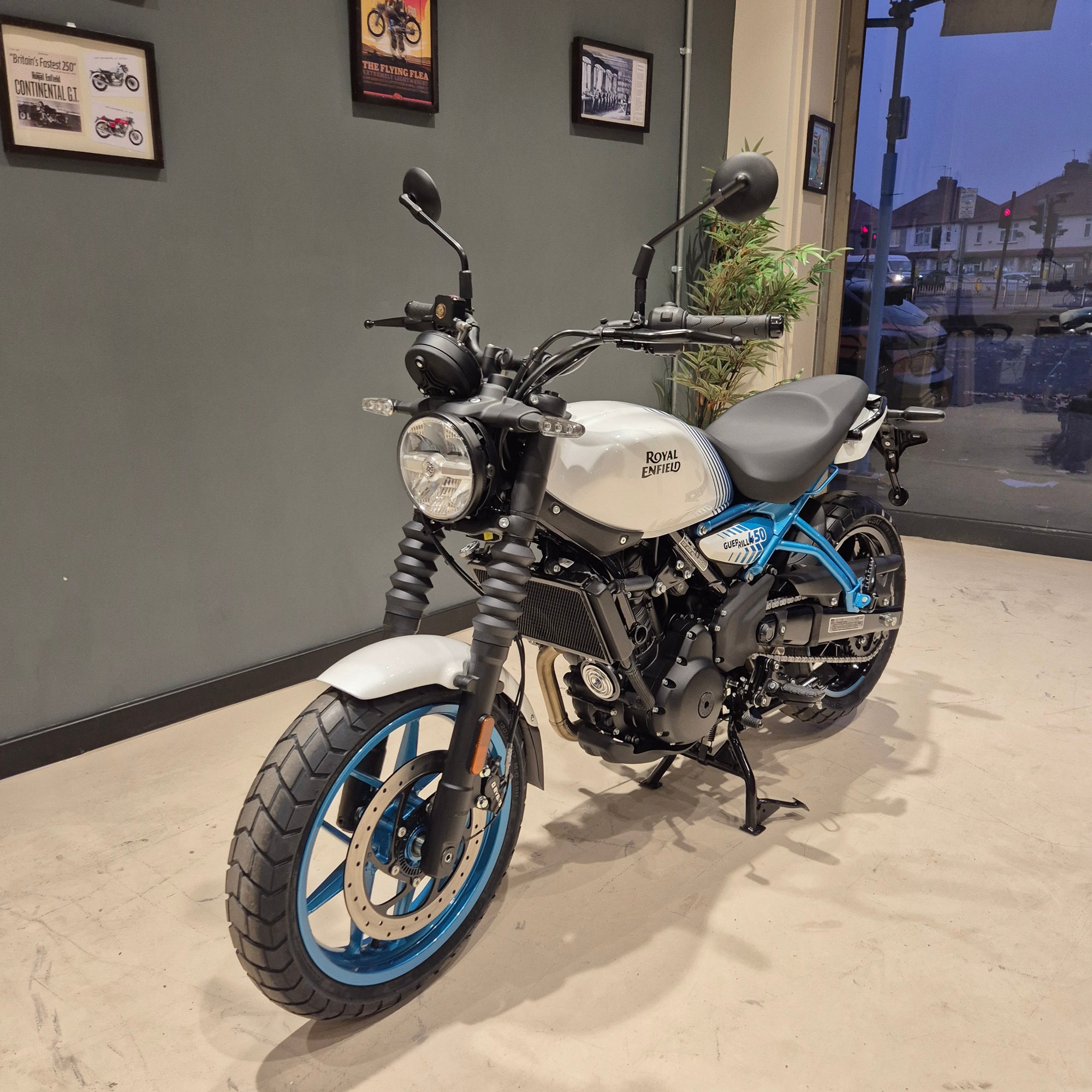 A Royal Enfield Classic 530 motorcycle with a white tank, black seat, and distinctive blue wheel accents, parked inside a showroom.