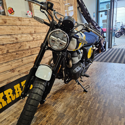 Motorcycle on display indoors with wooden floor and brick wall.