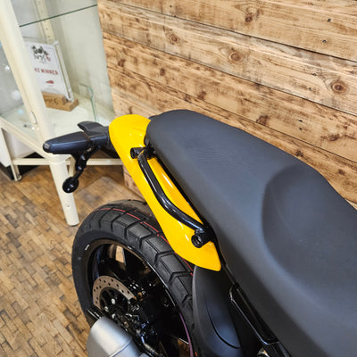 Close-up of a motorcycle seat and yellow fender on a wooden floor.