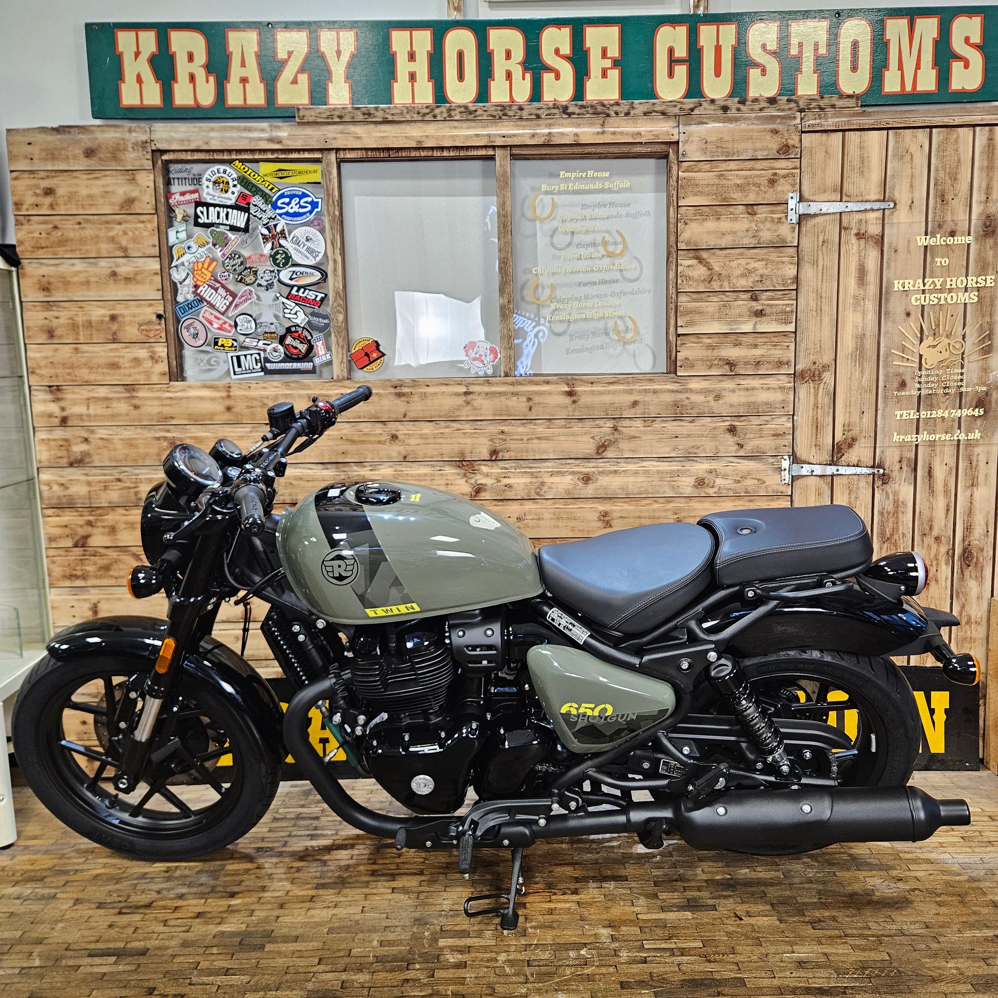 Motorcycle parked in front of a wooden wall with 'Krazy Horse Customs' sign.