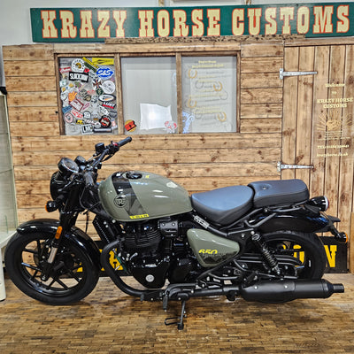 Motorcycle parked in front of a wooden wall with 'Krazy Horse Customs' sign.