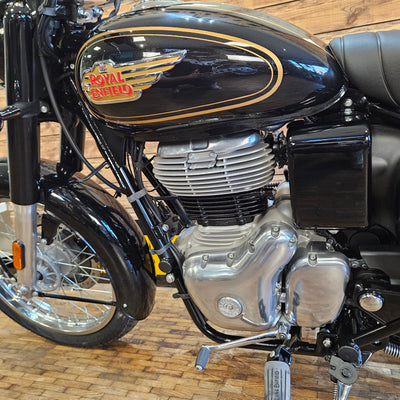 Close-up of a motorcycle engine and fuel tank with 'Royal Enfield' branding against a wooden background.