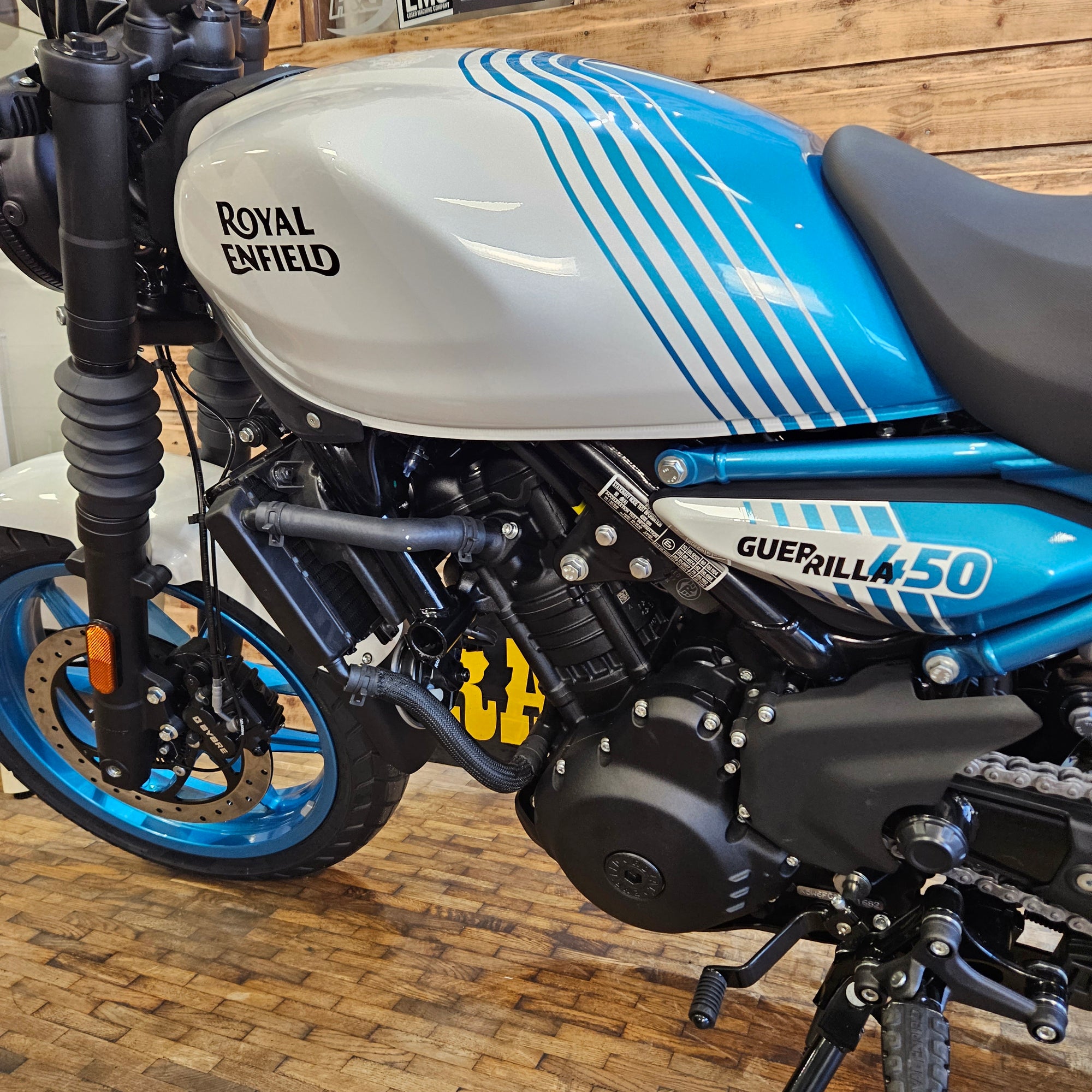 Close-up of a blue and white motorcycle with visible branding on a wooden floor.