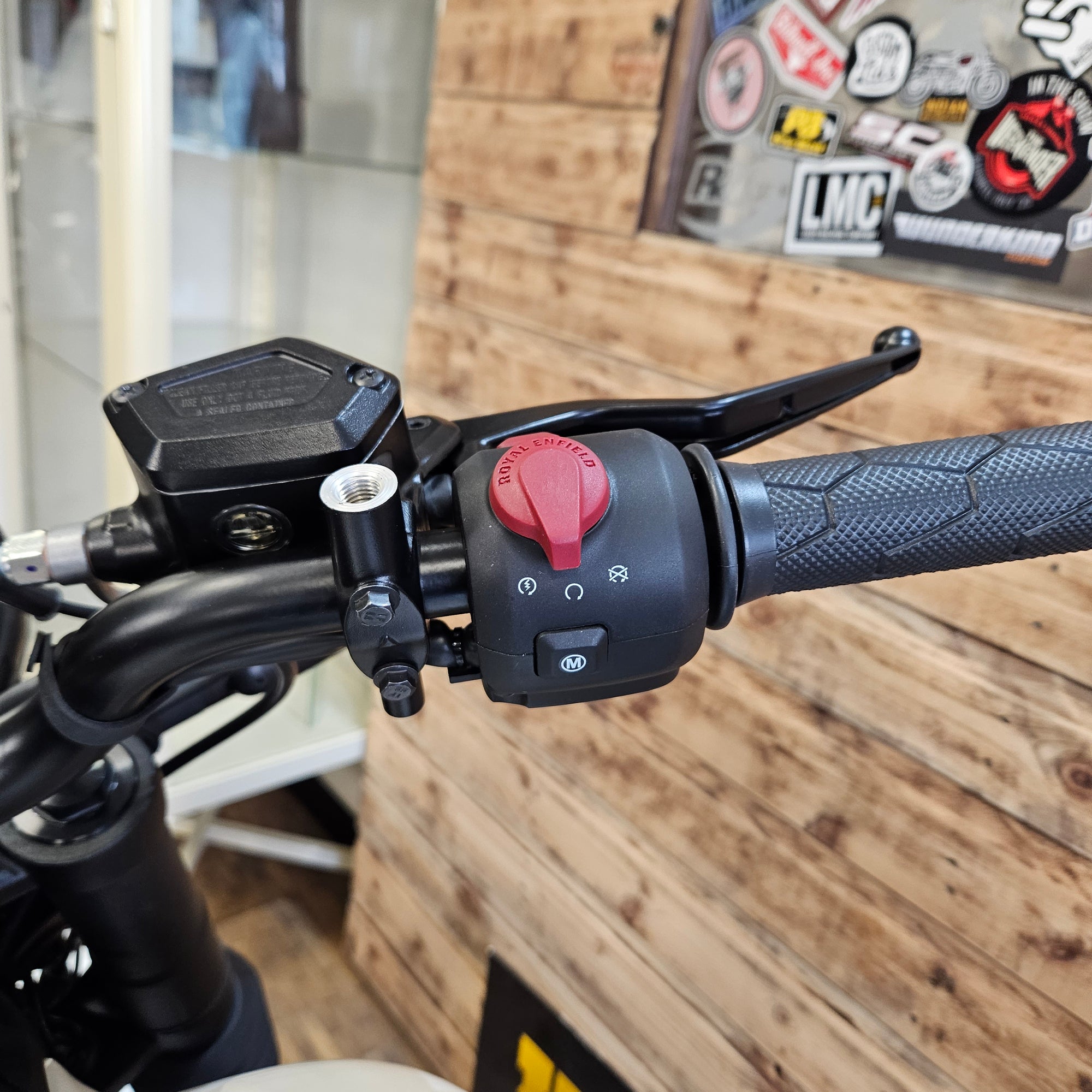 Close-up of a motorcycle handlebar with control buttons against a wooden wall background