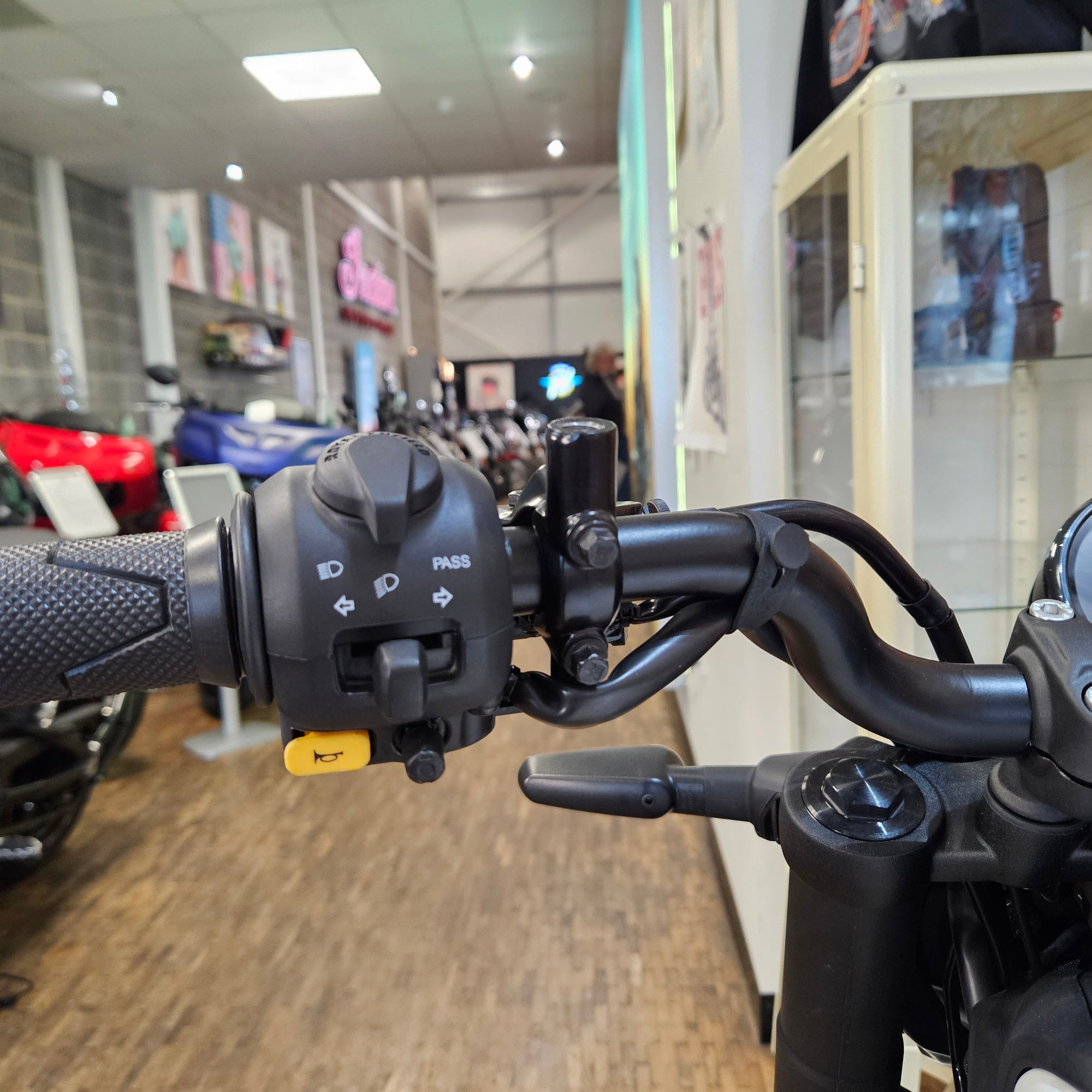 Close-up of a motorcycle handlebar with control buttons in an indoor setting.