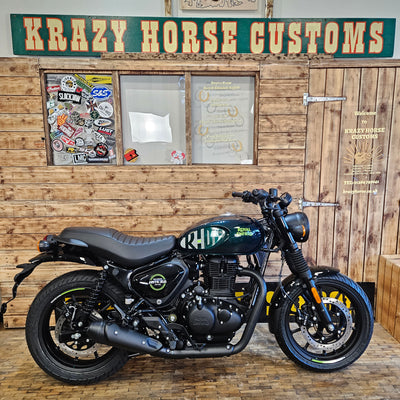 Motorcycle leaning against a wooden wall with 'Krazy Horse Customs' sign.
