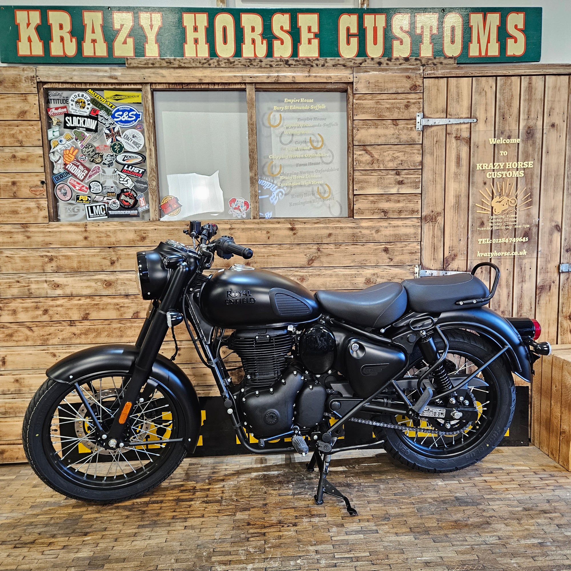 Black motorcycle leaning against a wooden wall with 'Krazy Horse Customs' sign.