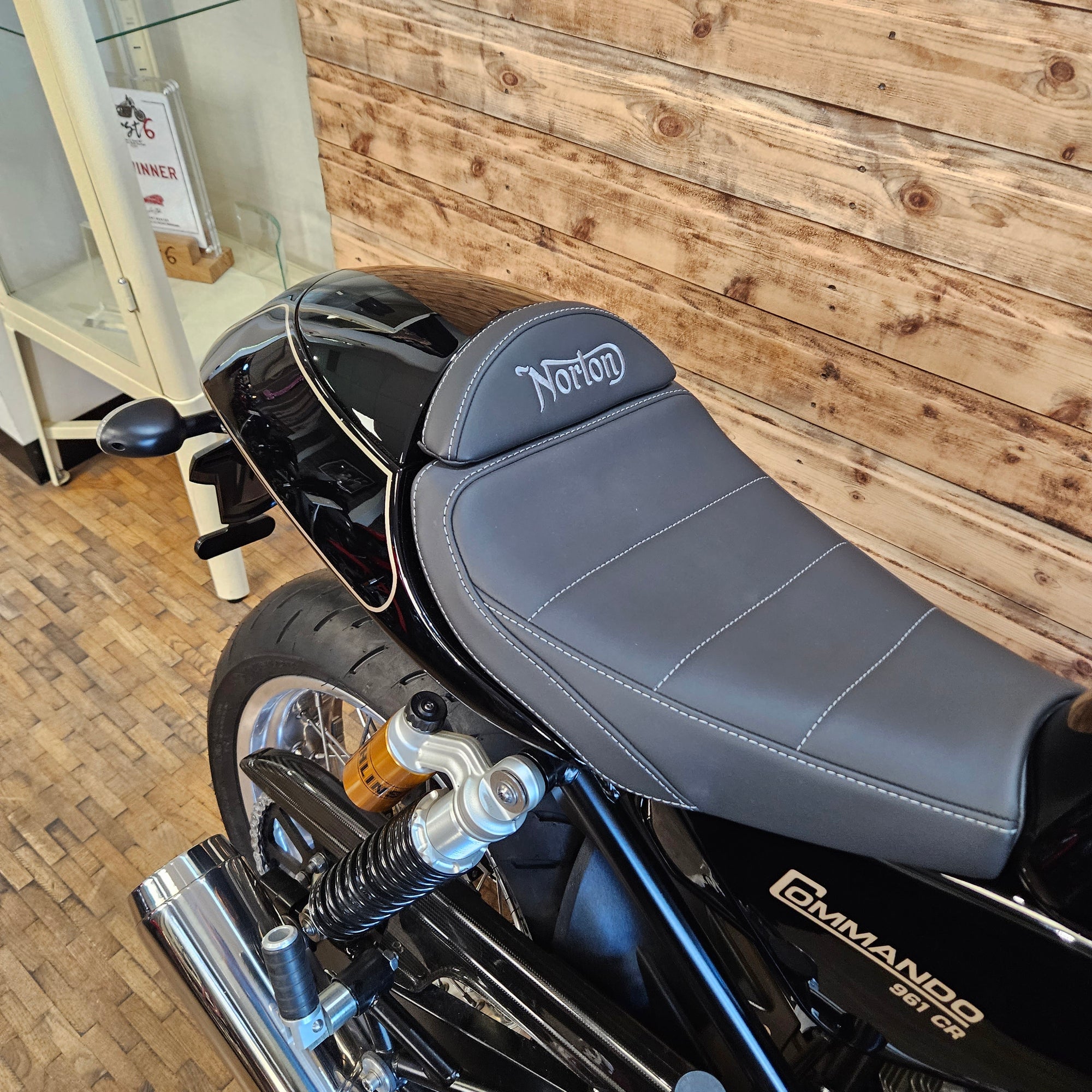 Gray motorcycle seat with 'Norton' branding on a wooden floor.