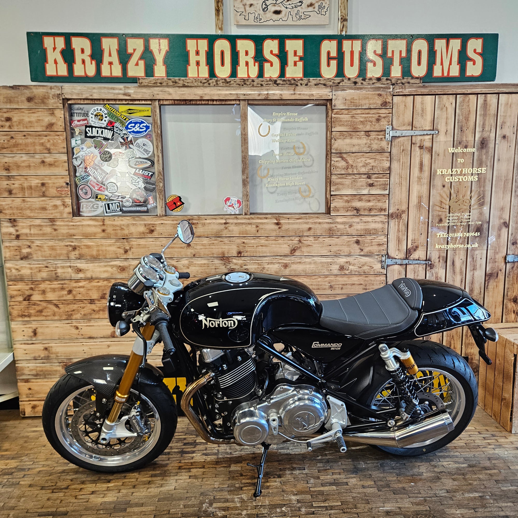 Black motorcycle on a wooden floor with 'Krazy Horse Customs' sign.
