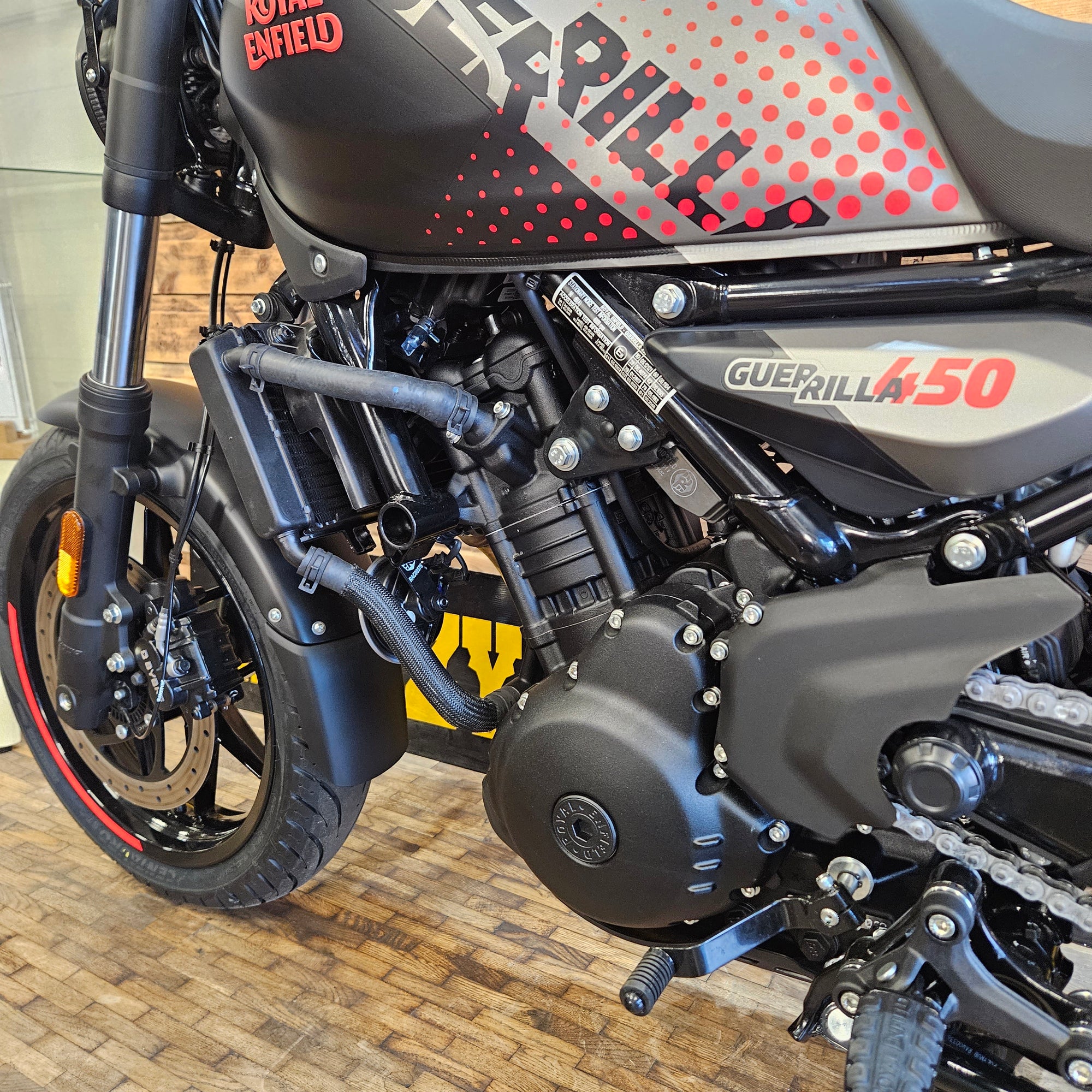 Close-up of a motorcycle engine and frame with visible branding on a wooden floor.