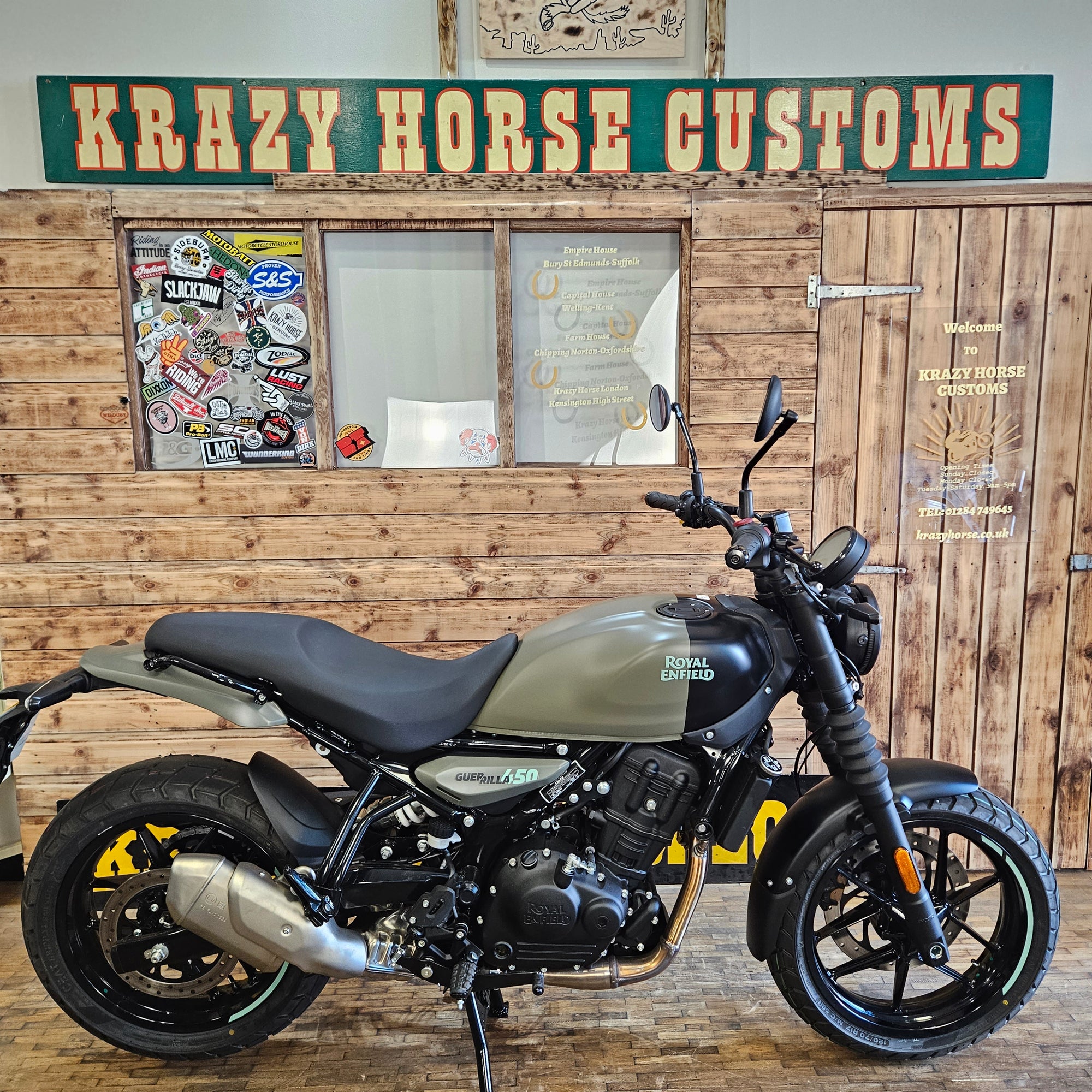 Motorcycle leaning against a wooden wall with 'Krazy Horse Customs' sign.