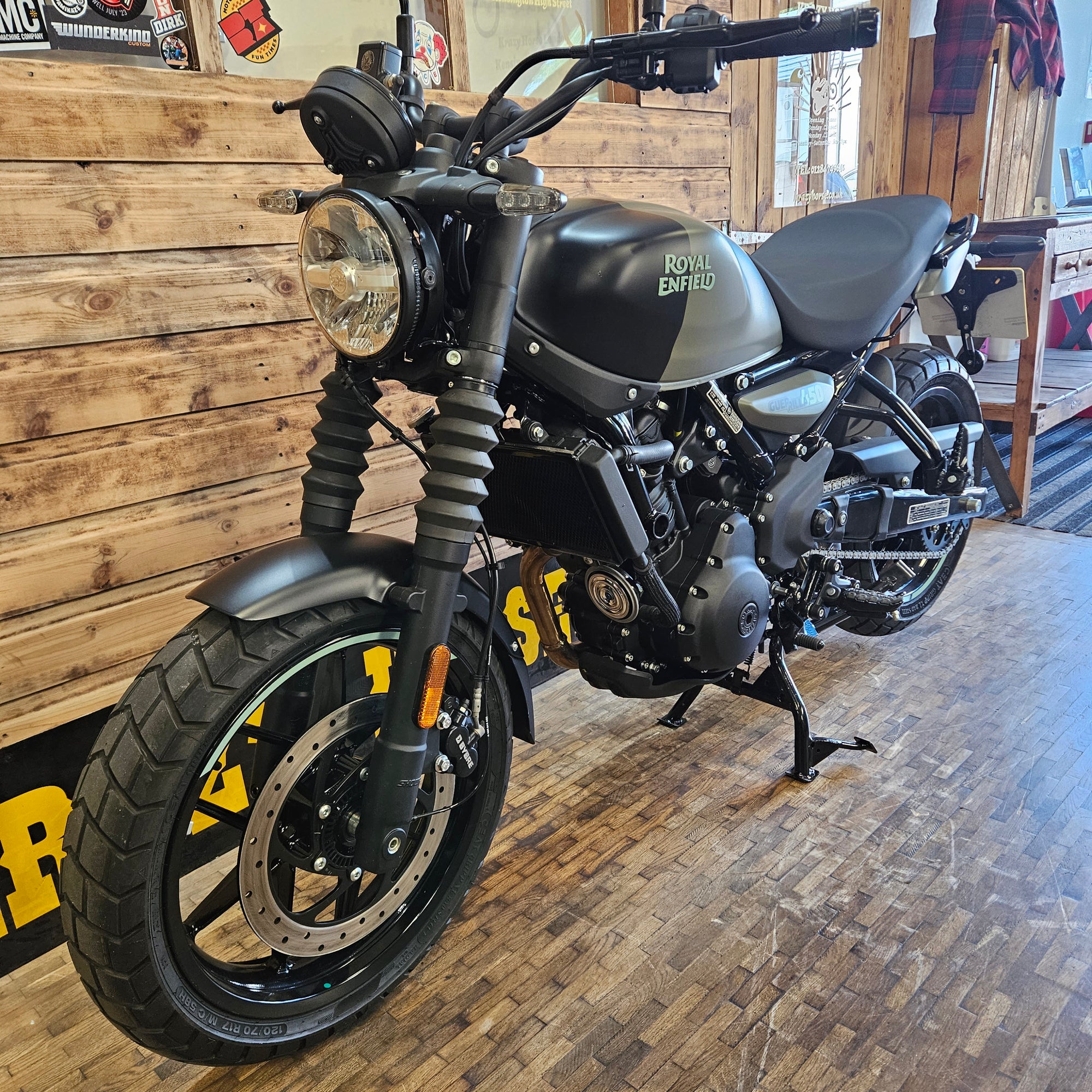 Black motorcycle with visible branding on a wooden floor against a brick wall.