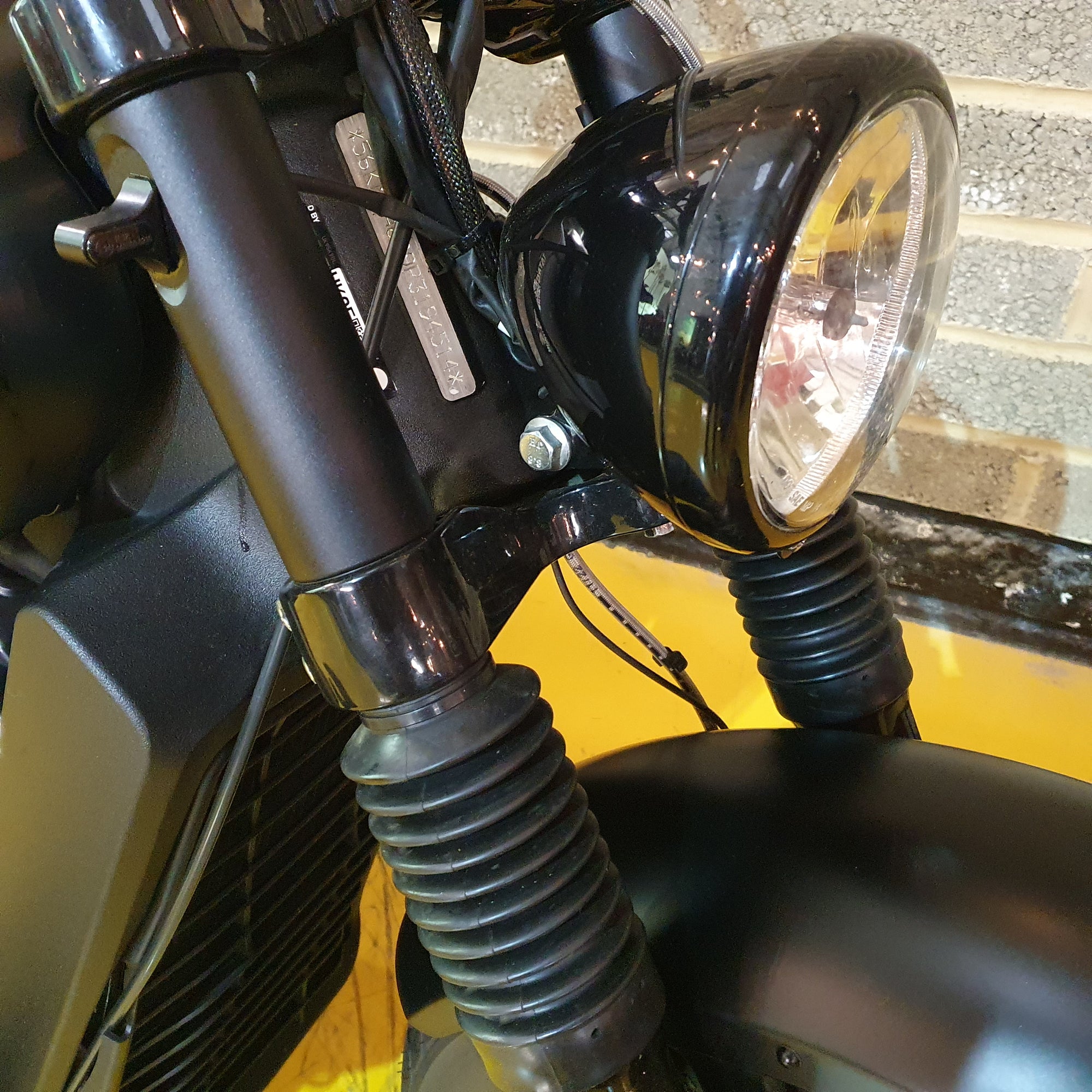 Close-up of a motorcycle headlight and handlebar on a yellow background