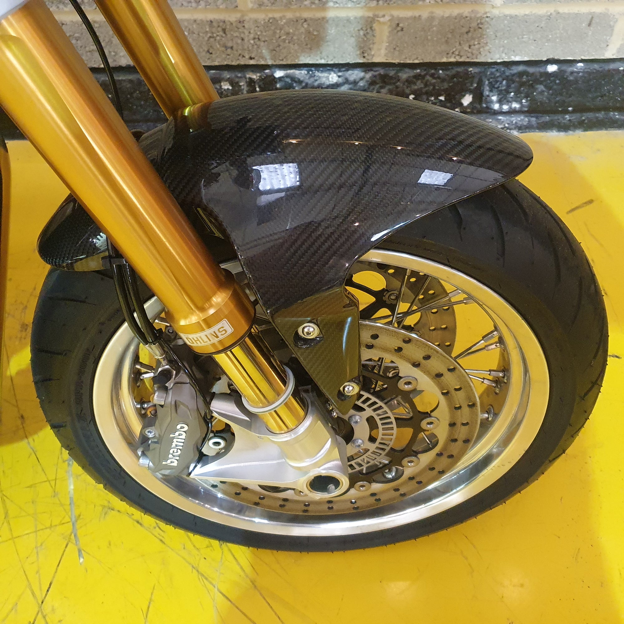 Close-up of a motorcycle wheel with gold suspension fork on a yellow background