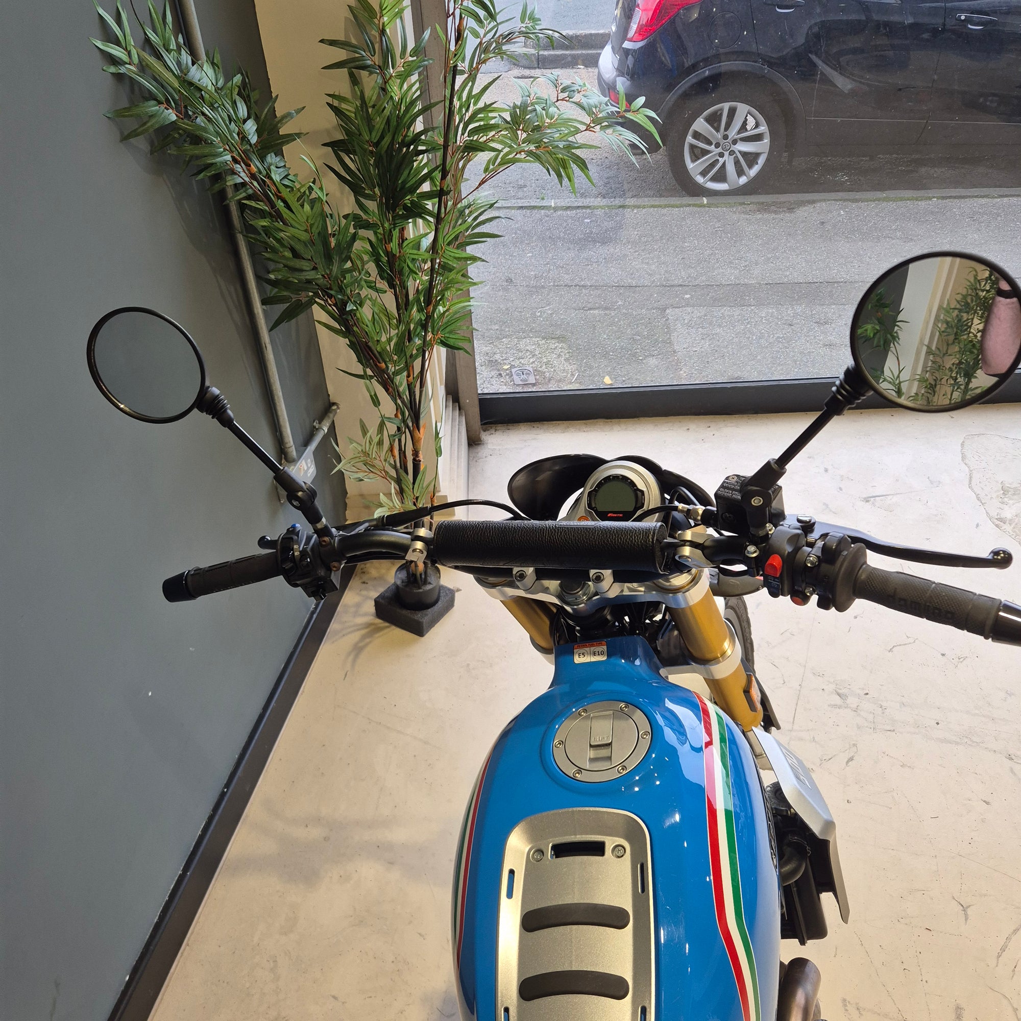 Blue scooter with Italian flag design indoors, near a window with plants.