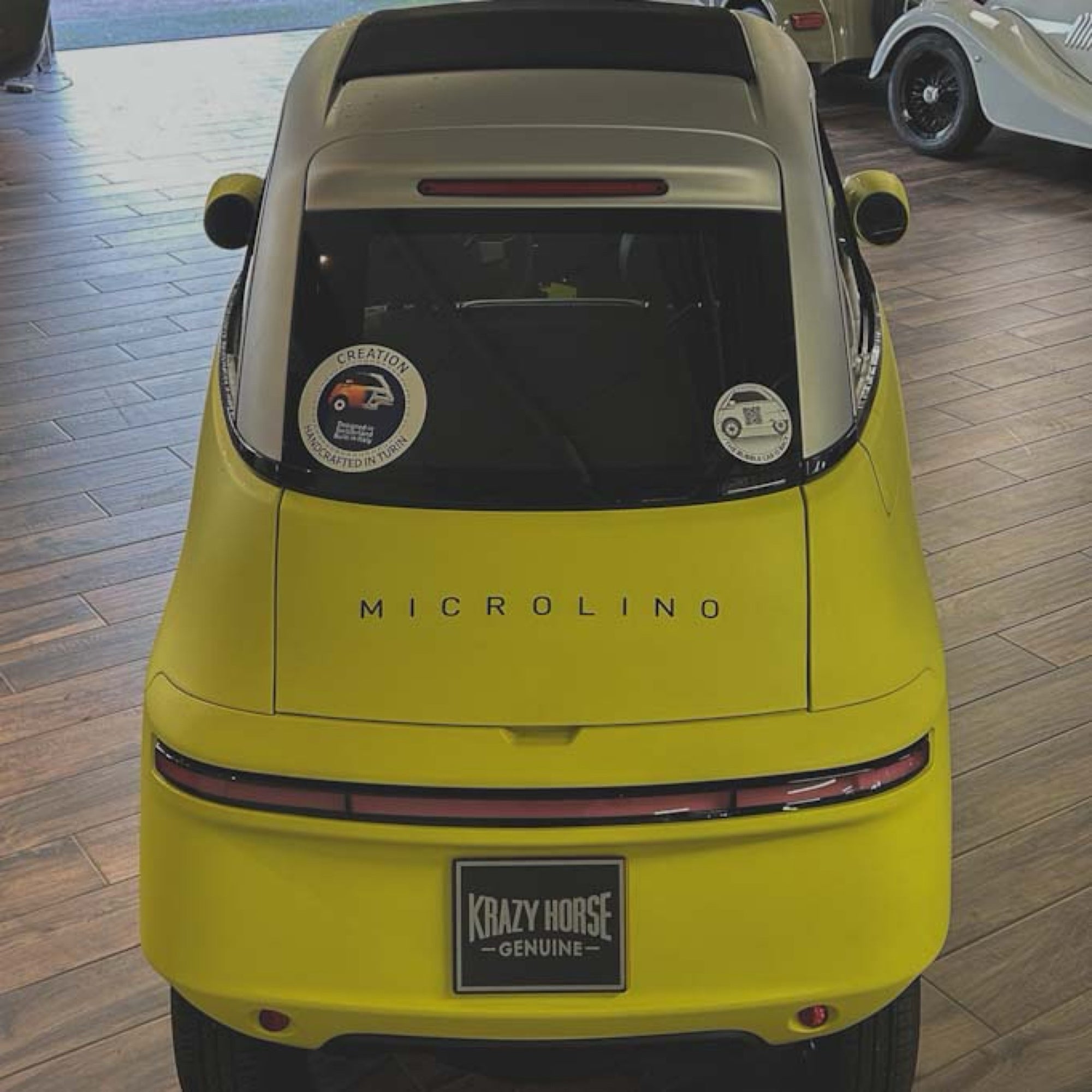Yellow Microlino car with 'Krazy Horse' license plate in a showroom.