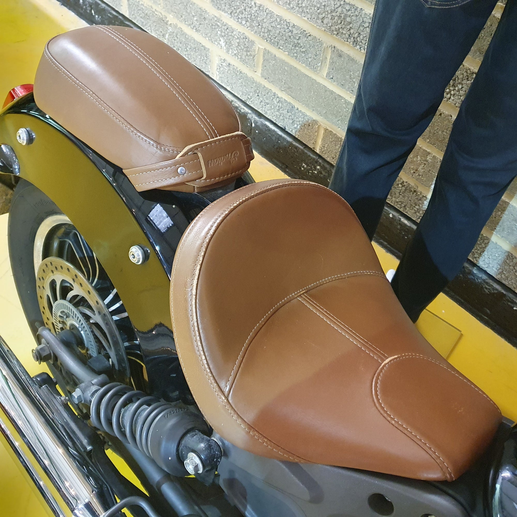 Close-up of a motorcycle seat with brown leather on a yellow bike, person partially visible.
