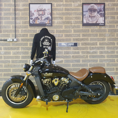Black Indian motorcycle with a person wearing a black hoodie in front of a brick wall with framed pictures.