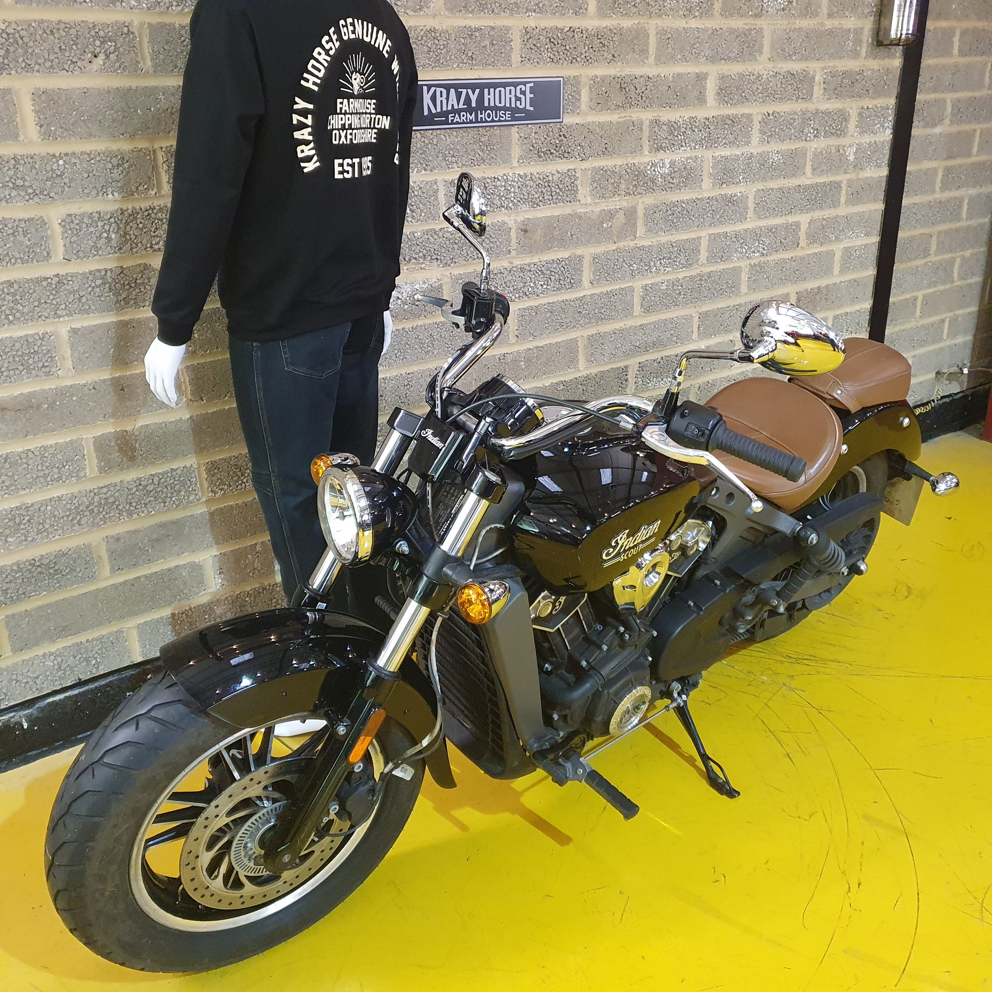 Motorcycle parked in front of a brick wall with a person wearing a black sweatshirt.