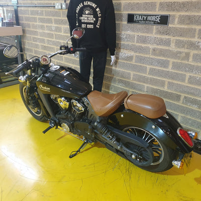 Black motorcycle with brown seat on a yellow floor against a brick wall.