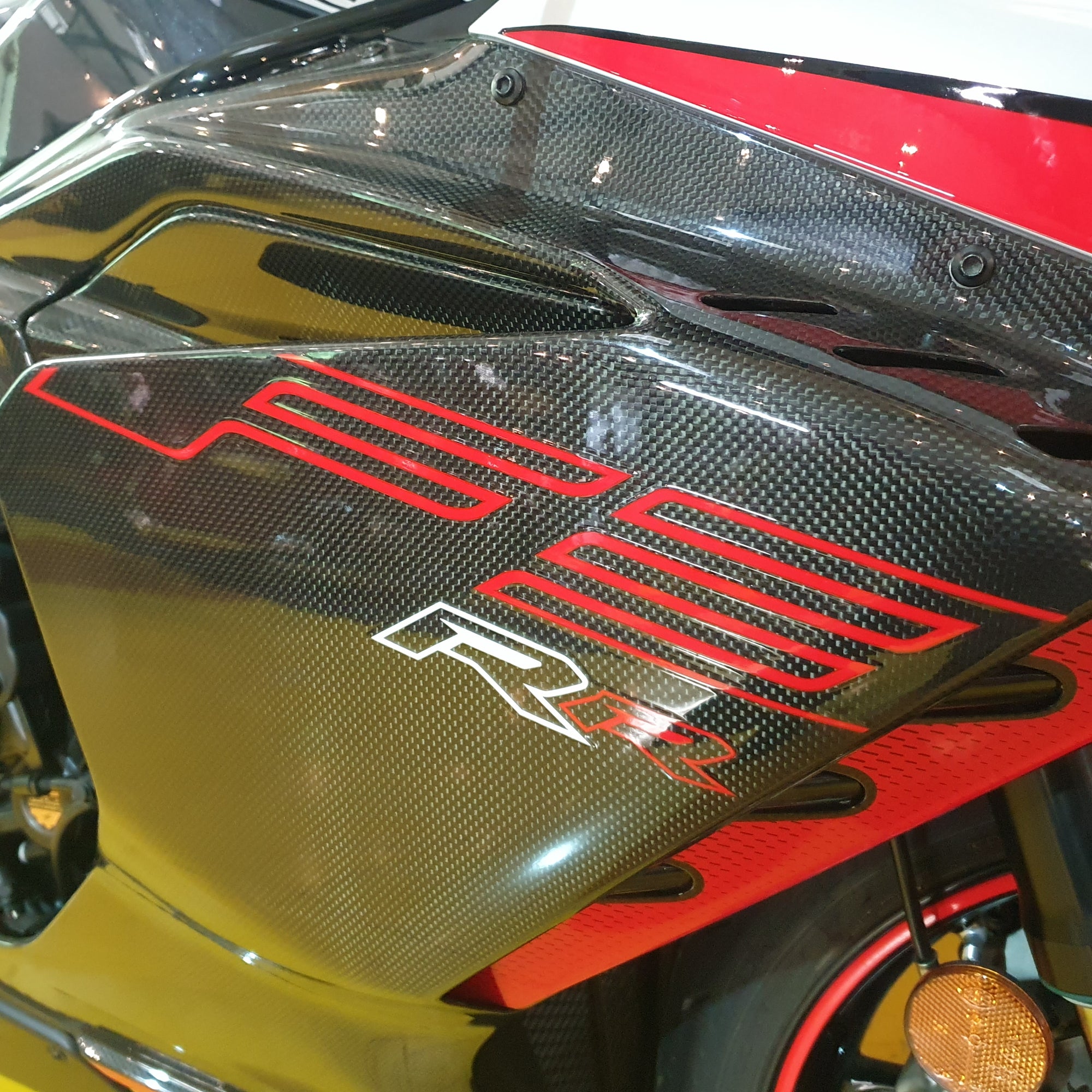 Close-up of a motorcycle with a carbon fiber finish and red branding.
