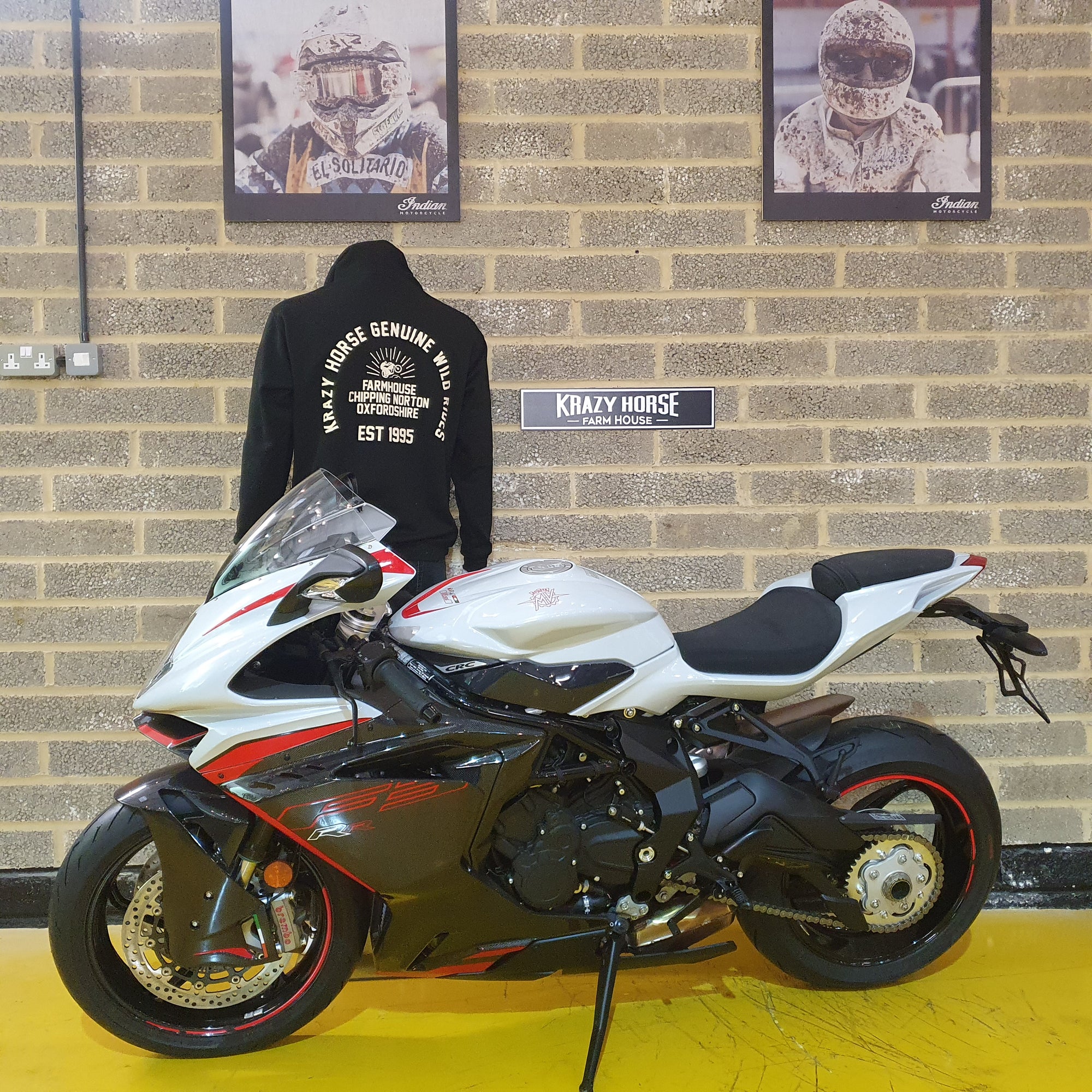 White motorcycle with black and red accents on a yellow floor against a brick wall.