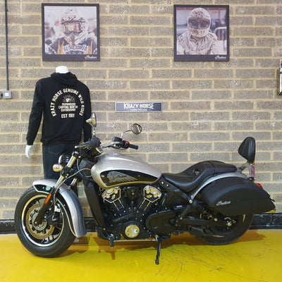 Motorcycle on display against a brick wall with framed pictures and a mannequin wearing a hoodie.