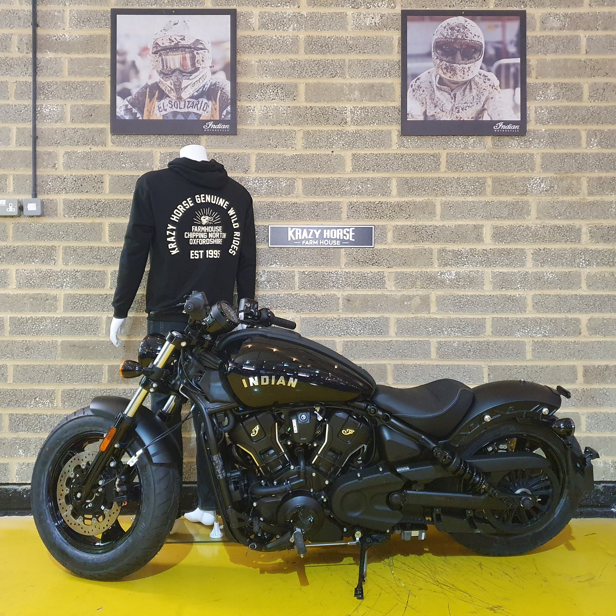 Black Indian motorcycle in a showroom with a brick wall and framed pictures.