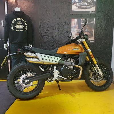 Orange and black motorcycle on display with a person wearing a branded hoodie in the background.