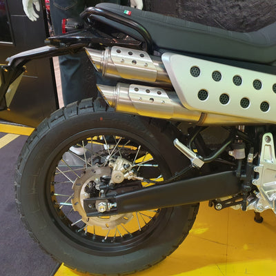 Close-up of a motorcycle's rear wheel and exhaust system on a showroom floor.