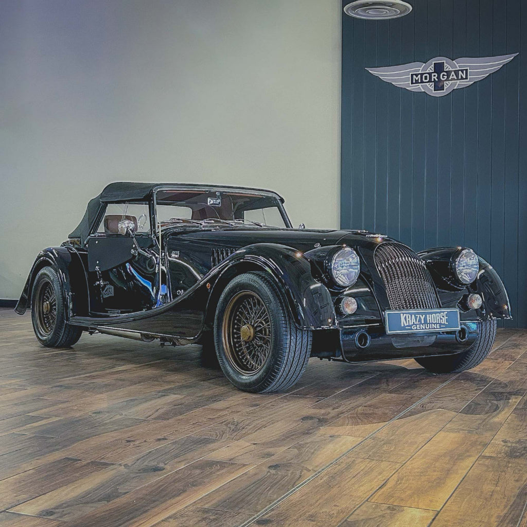 Vintage black car on a wooden floor with a blue wall featuring a logo in the background