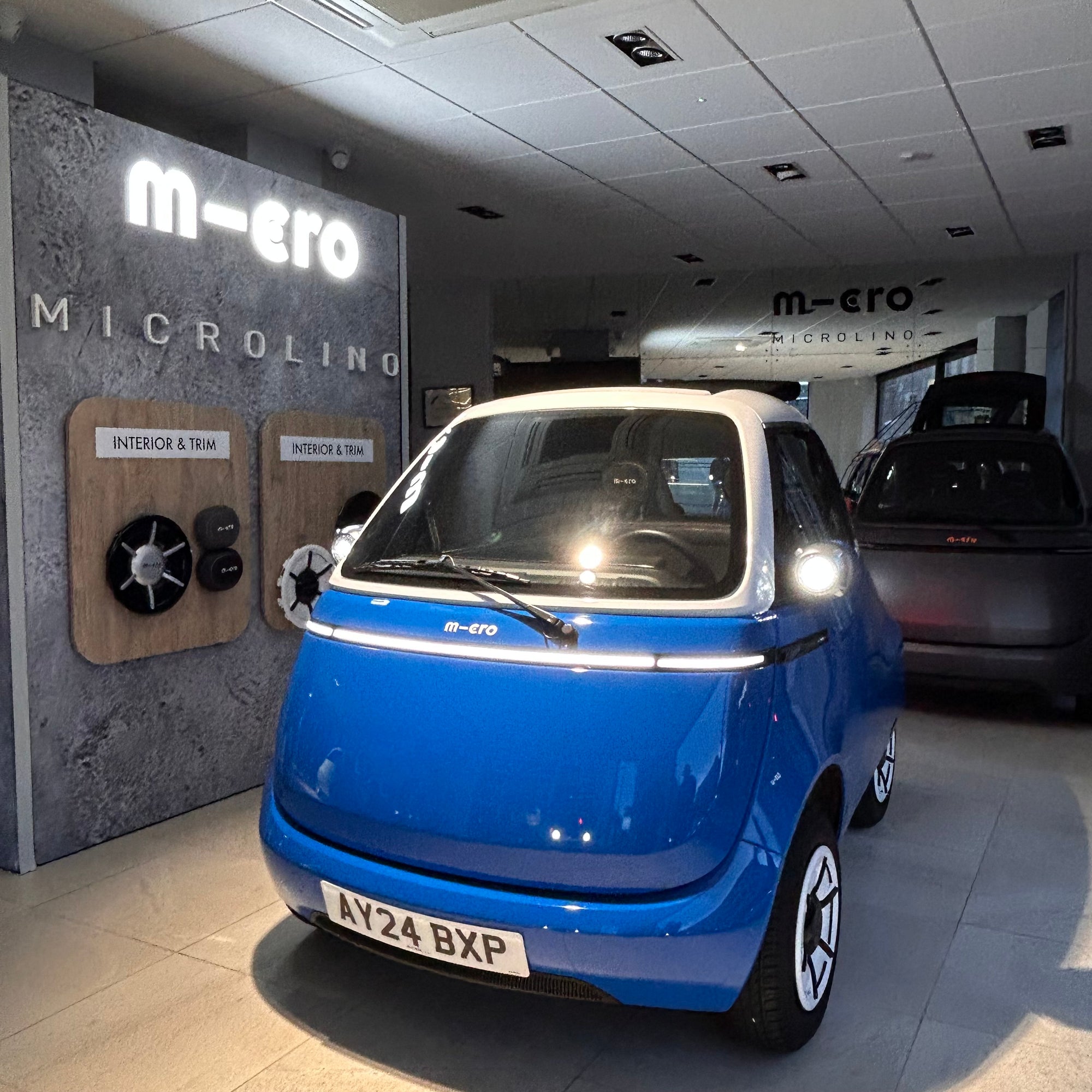 Blue microcar in a showroom with 'micro' branding on the wall.