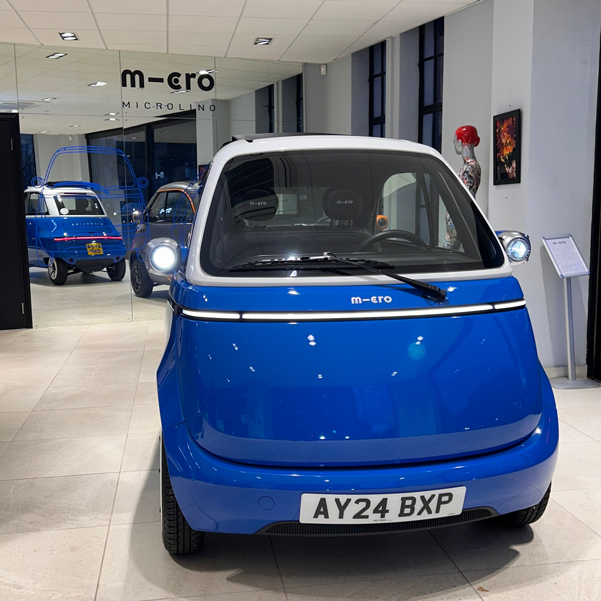 Blue microcar in a showroom with 'm-ero' branding.
