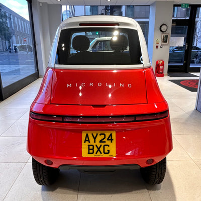 Red Microlino car inside a showroom with a yellow license plate.