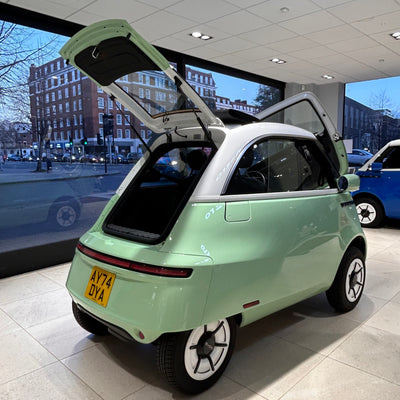 Small green car with open doors in a showroom