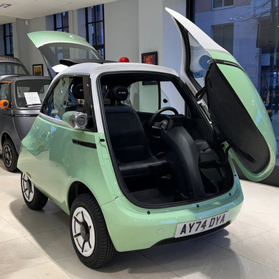 Small green car with open doors in a showroom