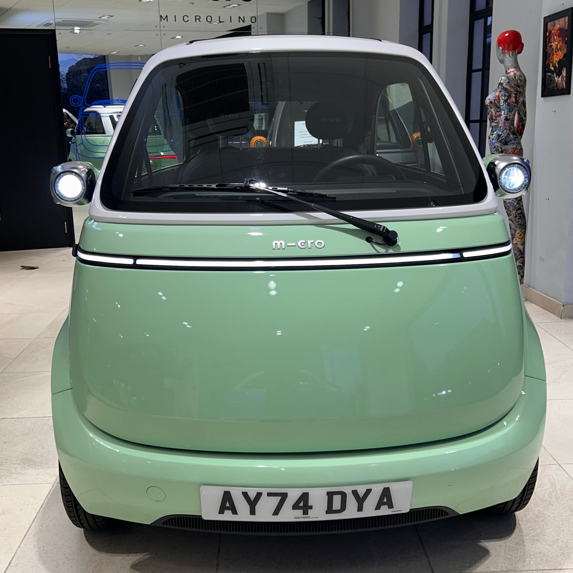 Small green car with 'Micro' branding inside a showroom.