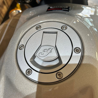 Close-up of a metallic fuel cap with a logo on a motorcycle.