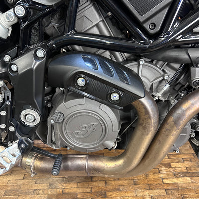 Close-up of a motorcycle engine and exhaust system on a wooden floor.