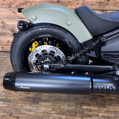Close-up of a motorcycle exhaust with 'Indian' branding on a wooden floor.