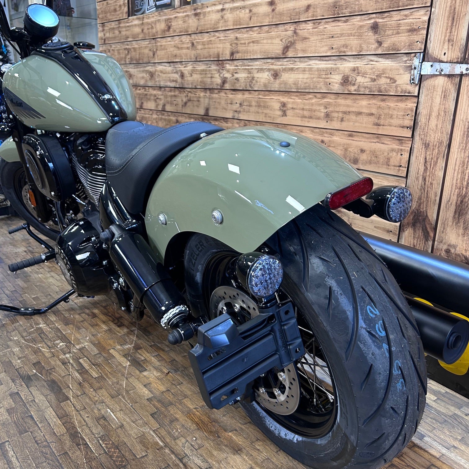 Green motorcycle parked indoors against a wooden wall.