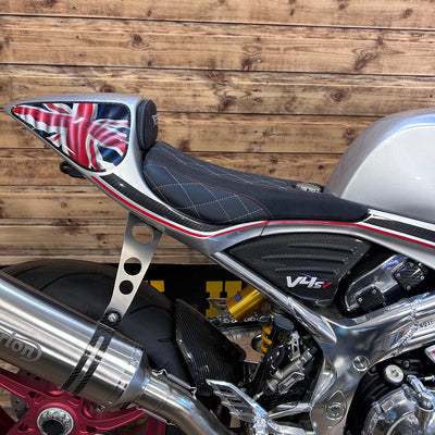 Motorcycle with a Union Jack design on the seat against a wooden wall.