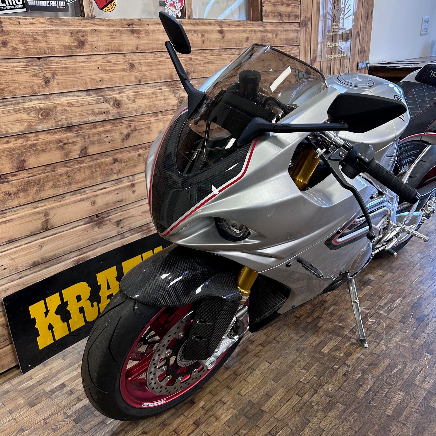 Silver motorcycle on display in a showroom with a wooden floor and 'Kraw' sign.