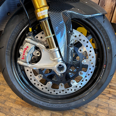 Close-up of a motorcycle wheel with brake disc and suspension fork on a wooden floor.