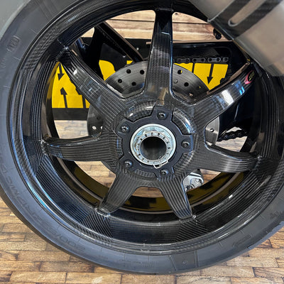 Close-up of a motorcycle wheel with a visible brand logo on a wooden floor.
