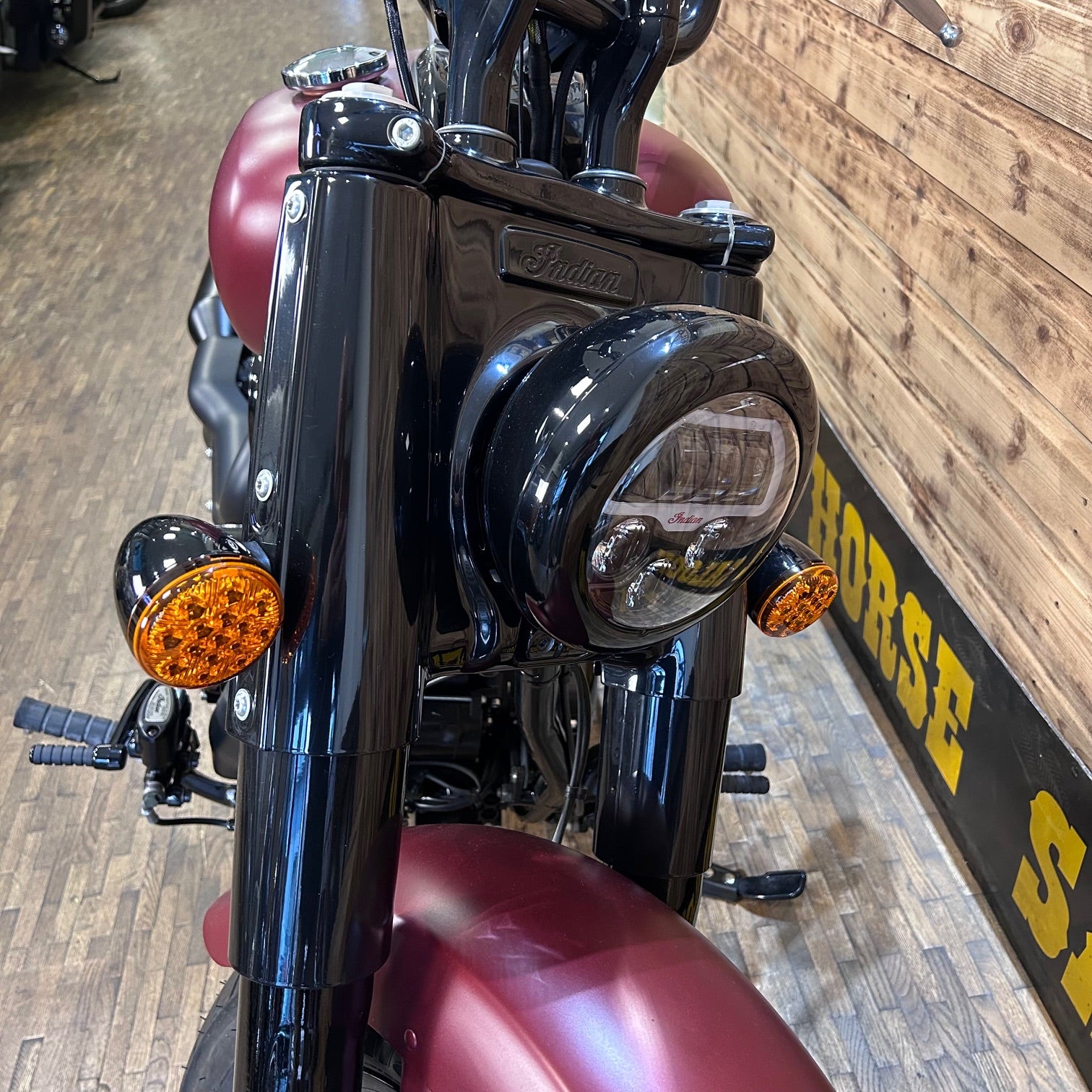 Close-up of a motorcycle's front headlight and turn signals with a wooden floor background.