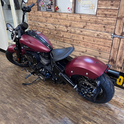 Maroon motorcycle parked indoors against a wooden wall.