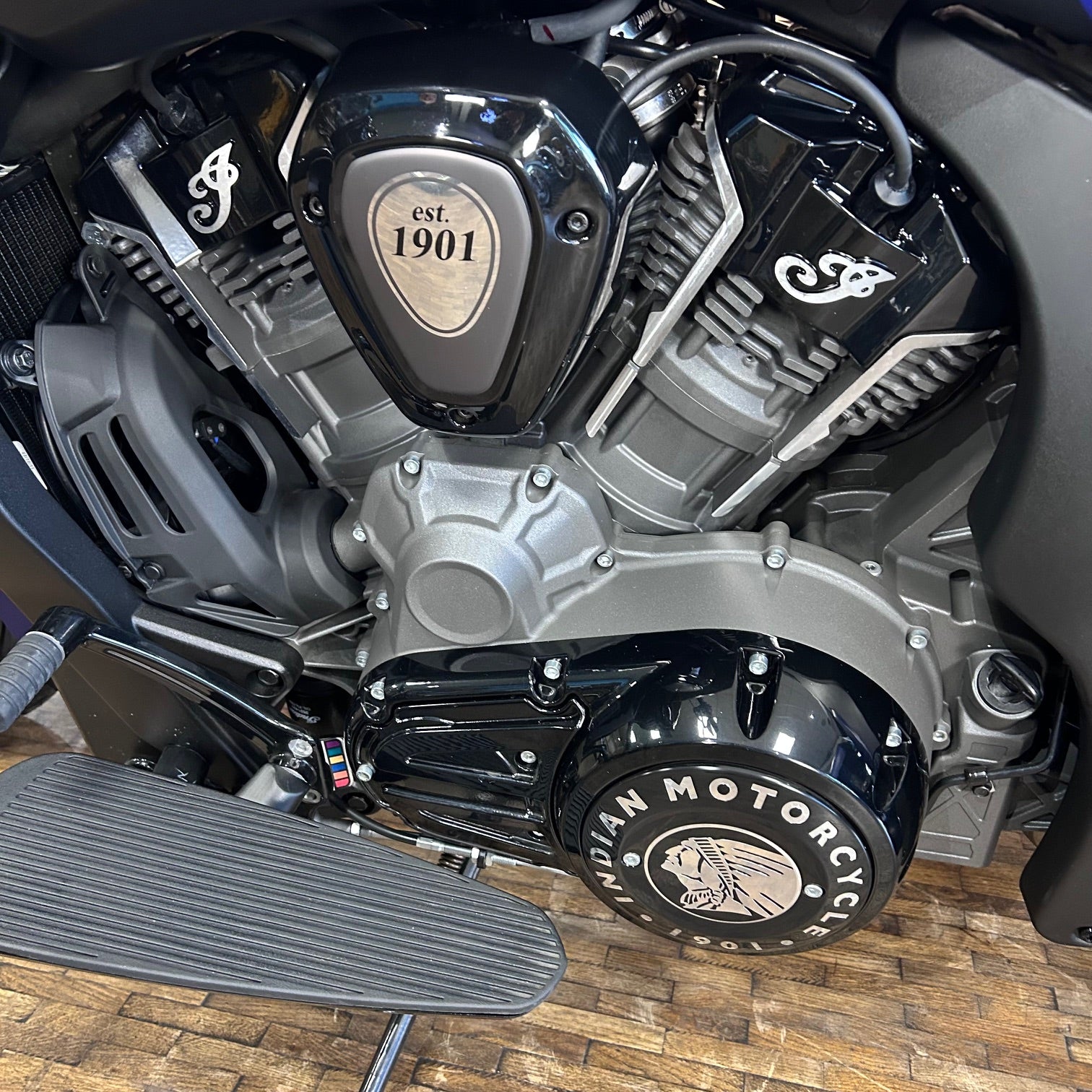Close-up of a motorcycle engine with 'Indian Motorcycle' branding on a wooden floor.