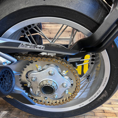 Close-up of a motorcycle wheel with sprocket and chain on a wooden floor.
