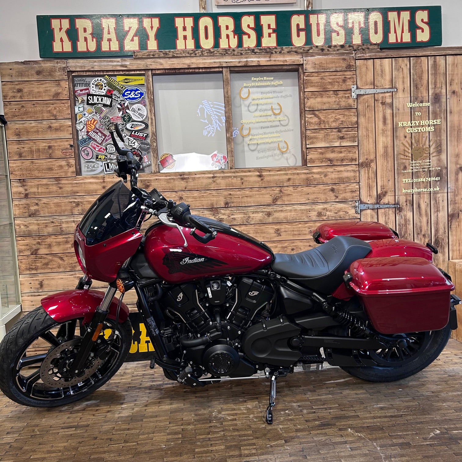 Red motorcycle with black seat and sidecar in front of a wooden building with 'Krazy Horse Customs' sign.